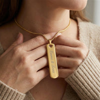 Femme tenant le collier barre verticale doré gravé